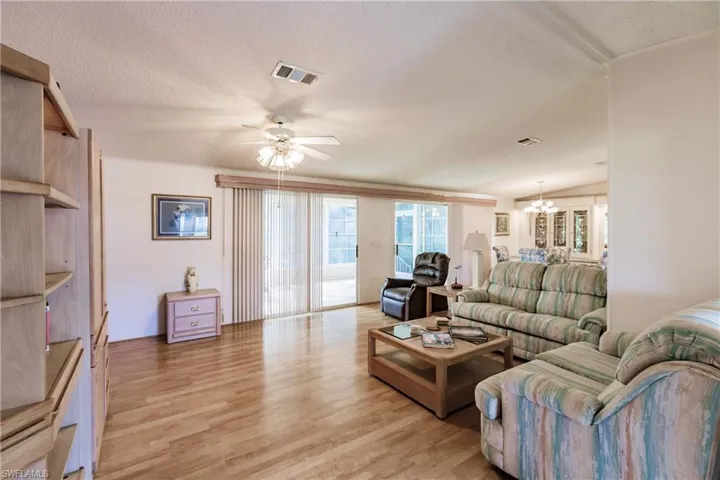 Living room featuring ceiling fan with notable chandelier, light wood-type flooring, and a textured ceiling