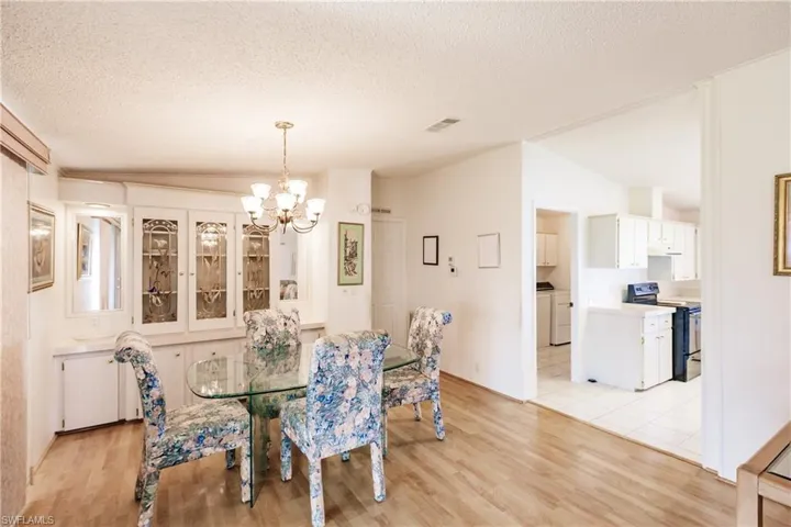 Dining area with an inviting chandelier, light wood-type flooring, lofted ceiling, washer / clothes dryer, and a textured ceiling