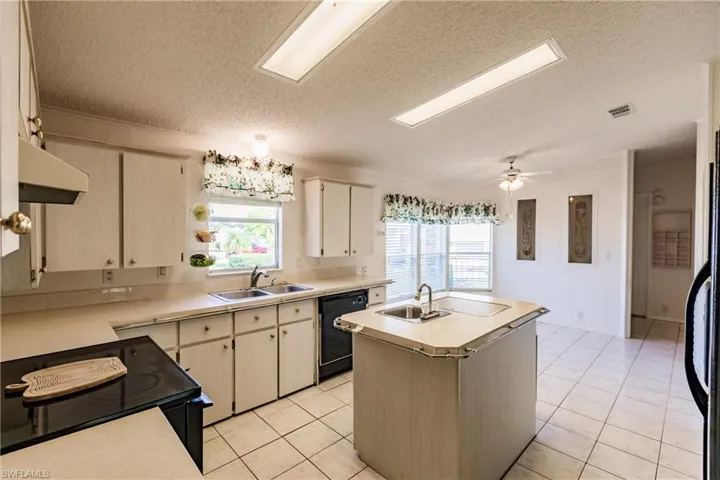 Kitchen with a textured ceiling, black appliances, an island with sink, ceiling fan, and sink