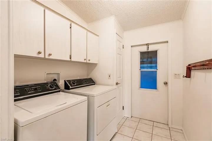 Laundry area featuring crown molding, washer and dryer, light tile patterned flooring, cabinets, and a textured ceiling