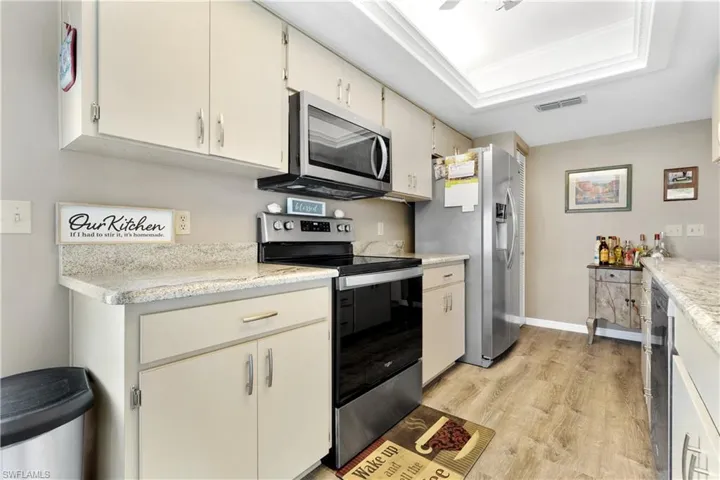 Kitchen with appliances with stainless steel finishes, light wood-type flooring, a raised ceiling, and cream cabinetry
