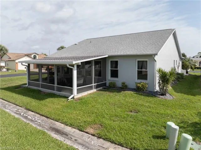 Rear view of house featuring roof with shingles, a yard, stucco siding, and a sunroom