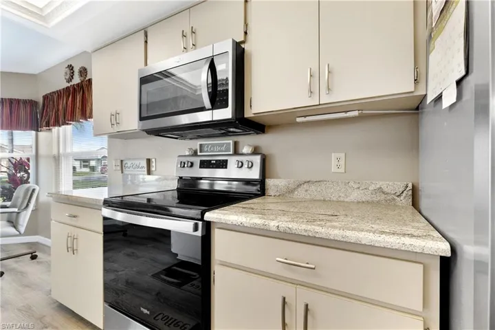 Kitchen with stainless steel appliances, cream cabinetry, light wood-style floors, and light stone counters
