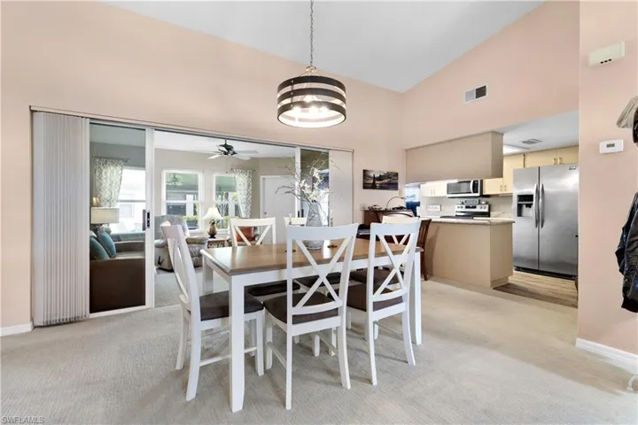Dining room with light carpet, ceiling fan, high vaulted ceiling, and a chandelier