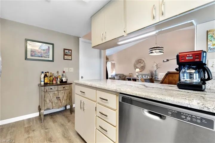 Kitchen with cream cabinets, dishwasher, light wood-style flooring, decorative light fixtures, and light stone countertops