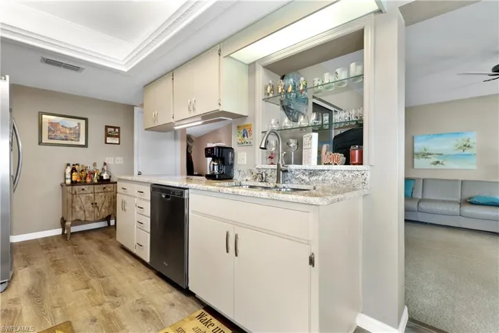 Kitchen featuring dishwasher, light wood-type flooring, light stone countertops, freestanding refrigerator, and ornamental molding