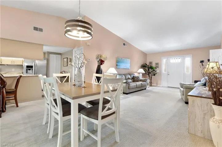Dining space featuring light colored carpet, vaulted ceiling, and a chandelier