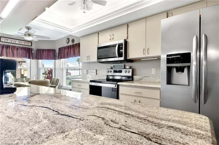 Kitchen with appliances with stainless steel finishes, cream cabinetry, ceiling fan, light stone counters, and crown molding