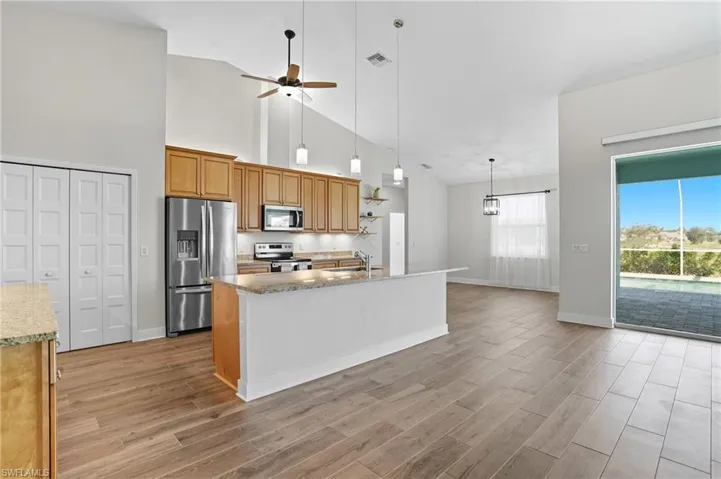 Kitchen with appliances with stainless steel finishes, light stone countertops, pendant lighting, ceiling fan, and light wood-type flooring