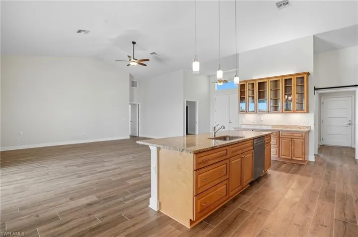 Kitchen with glass insert cabinets, light stone countertops, open floor plan, pendant lighting, and a center island with sink