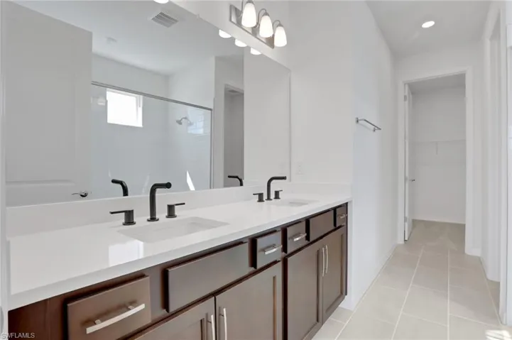 Full bathroom with double vanity, a stall shower, a spacious closet, light tile patterned floors, and recessed lighting