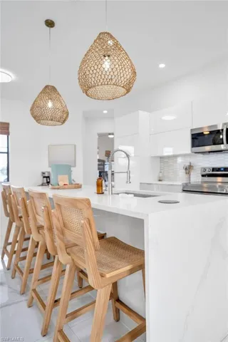 Kitchen with modern cabinets, a kitchen breakfast bar, hanging light fixtures, tasteful backsplash, and appliances with stainless steel finishes