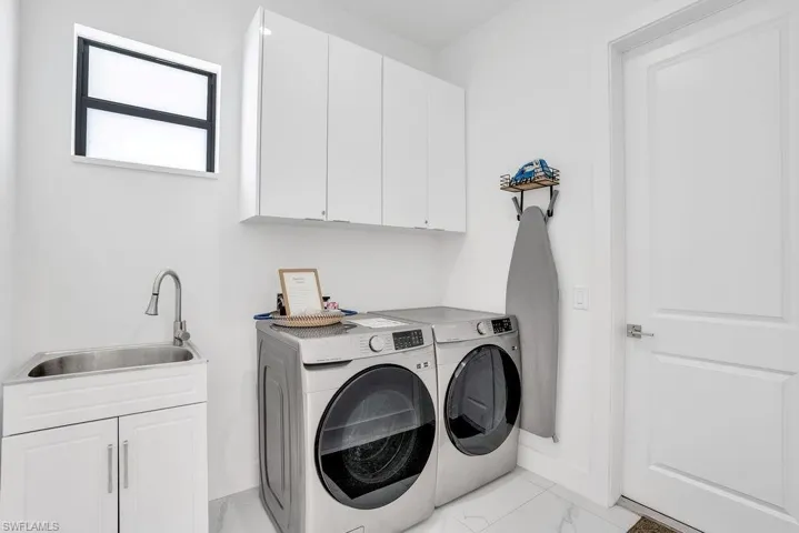 Laundry area with cabinet space, light marble finish flooring, and washing machine and dryer