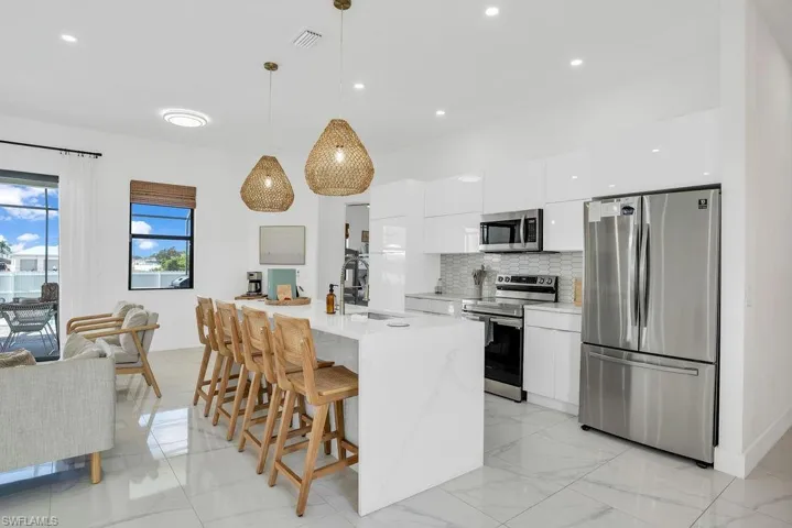 Kitchen featuring appliances with stainless steel finishes, white cabinetry, modern cabinets, tasteful backsplash, and hanging light fixtures