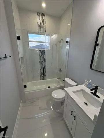 Full bath featuring shower / bath combination with glass door, vanity, and light marble finish flooring