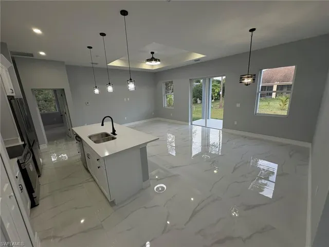 Kitchen with a tray ceiling, open floor plan, an island with sink, and white cabinetry