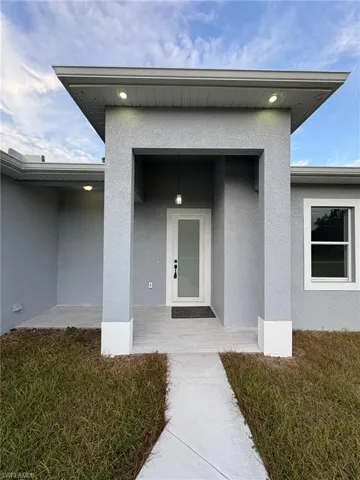 Property entrance with covered porch, stucco siding, and a lawn