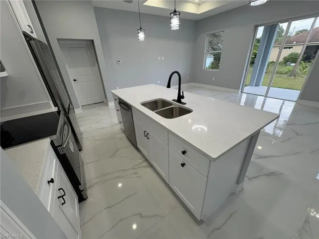 Kitchen featuring light marble finish floors, light stone counters, hanging light fixtures, and a center island with sink
