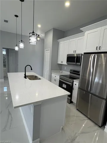 Kitchen featuring appliances with stainless steel finishes, light marble finish floors, white cabinets, light stone counters, and recessed lighting