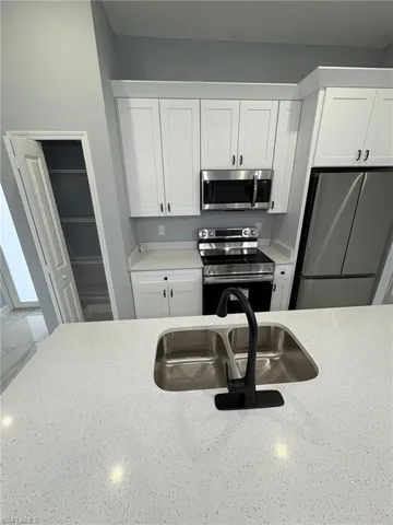 Kitchen with stainless steel appliances, white cabinets, and light stone counters