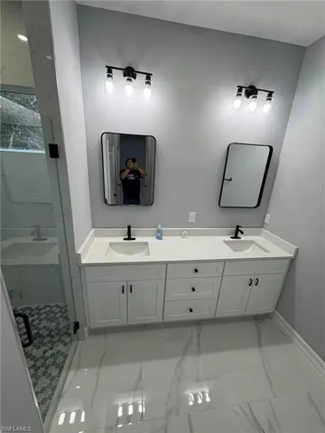 Bathroom with light marble finish flooring, double vanity, and a marble finish shower