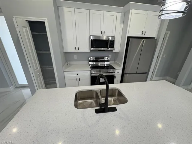 Kitchen featuring appliances with stainless steel finishes, white cabinets, light stone countertops, and decorative light fixtures