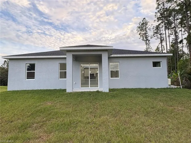 Rear view of property featuring a yard, stucco siding, and a shingled roof