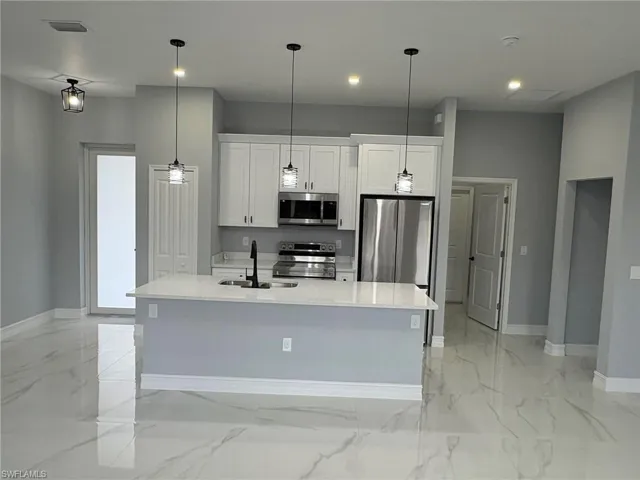 Kitchen with white cabinets, light stone counters, stainless steel appliances, a center island with sink, and decorative light fixtures