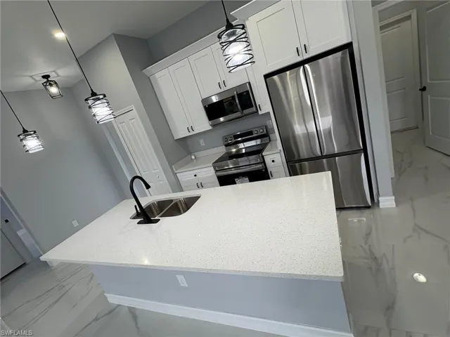 Kitchen featuring light marble finish flooring, decorative light fixtures, light stone counters, and stainless steel appliances
