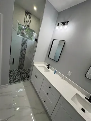 Full bathroom featuring light marble finish floors, a marble finish shower, and double vanity