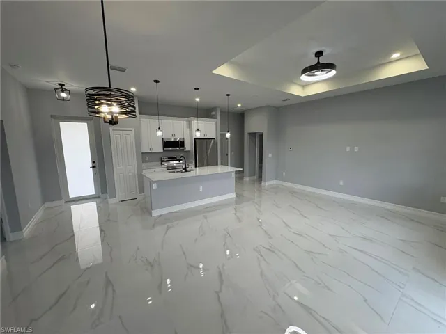 Kitchen with open floor plan, a kitchen island with sink, white cabinets, stainless steel appliances, and light marble finish flooring