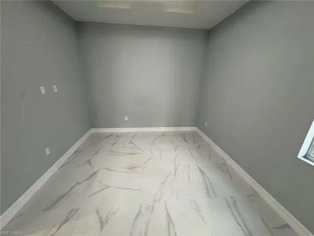 Unfurnished room featuring marble look tile flooring and baseboards