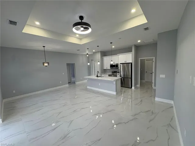 Unfurnished living room with a tray ceiling, recessed lighting, ceiling fan, and light marble finish flooring
