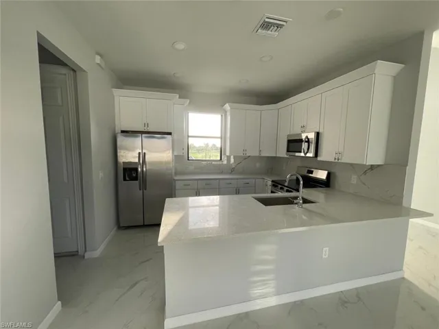 Kitchen with appliances with stainless steel finishes, light tile patterned floors, white cabinets, and tasteful backsplash