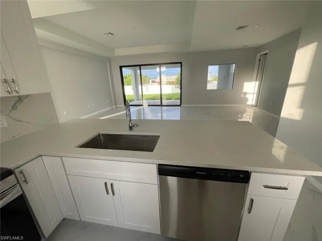 Kitchen featuring sink, kitchen peninsula, light stone counters, white cabinetry, and dishwasher