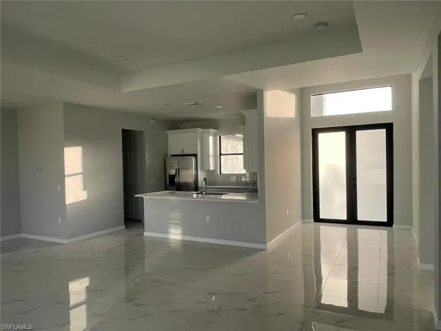 Unfurnished living room featuring sink, french doors, a raised ceiling, and light tile patterned floors