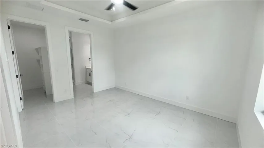 Unfurnished bedroom featuring light marble finish floors, a walk in closet, ensuite bathroom, and ceiling fan
