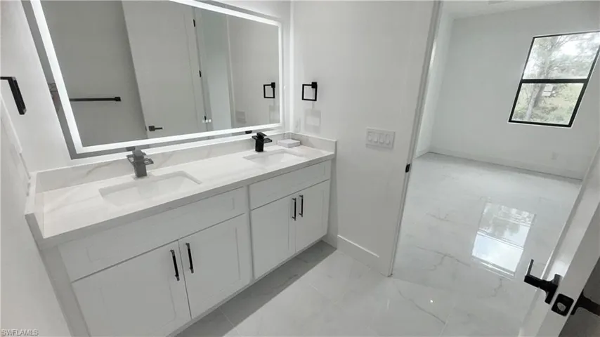 Full bath featuring double vanity and light marble finish flooring