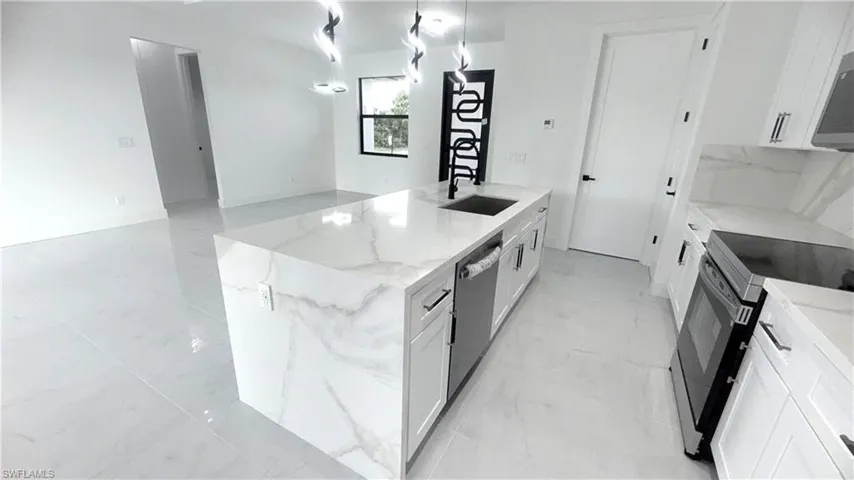 Kitchen with light stone counters, white cabinetry, appliances with stainless steel finishes, and light marble finish floors