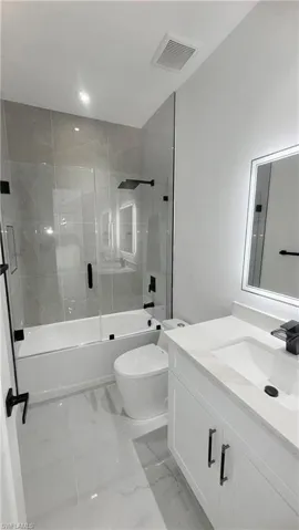 Bathroom featuring enclosed tub / shower combo, vanity, light marble finish flooring, and recessed lighting