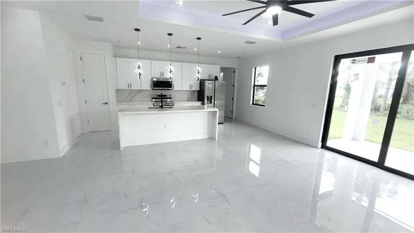Kitchen featuring pendant lighting, a tray ceiling, light marble finish floors, and white cabinets