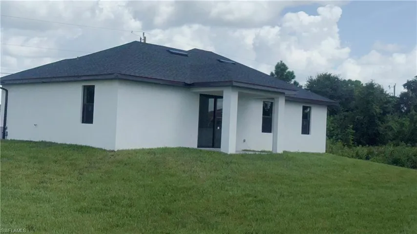 Rear view of house with roof with shingles, a yard, and stucco siding