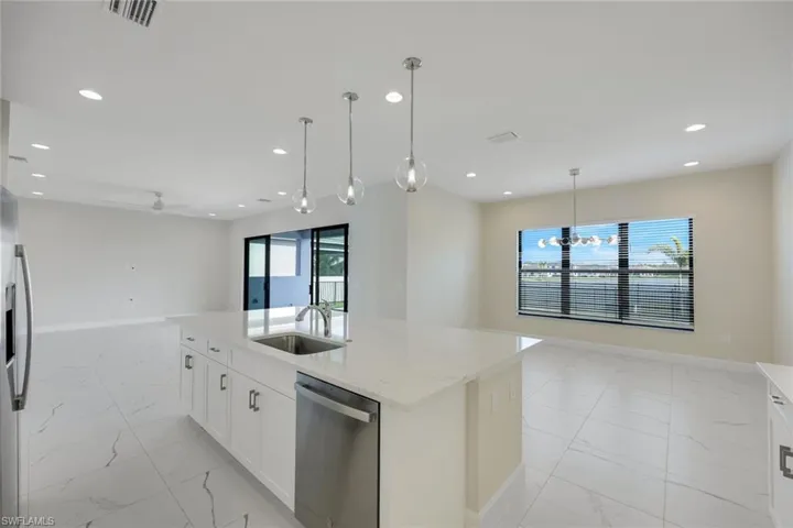 Kitchen with light stone countertops, appliances with stainless steel finishes, white cabinetry, sink, and a center island with sink