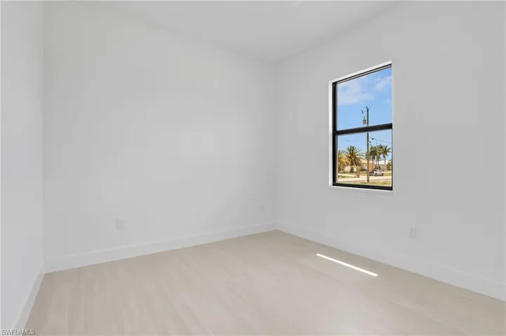 Bright interior space featuring a single window with black framing, light wood-finish flooring, white walls, and contemporary white baseboards