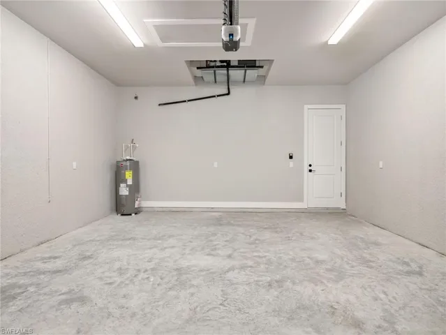 Spacious garage featuring a concrete floor, light gray walls, built-in water heater, interior access door, and overhead lighting