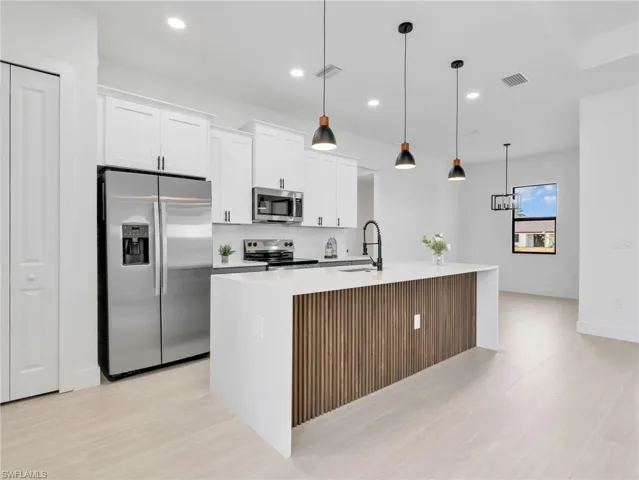 Contemporary kitchen featuring a waterfall island with a slatted wood-finish accent panel, quartz countertops, and stainless steel appliances