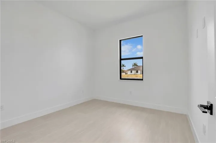 Bright interior room featuring a single window, light wood-finish flooring, white baseboards, and a contemporary door handle