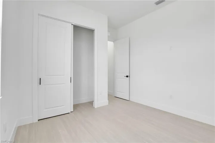 Room featuring light-toned flooring, white walls, and a white sliding closet door with dark hardware