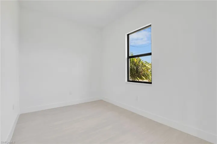 Bright interior space featuring a window with black trim, light-toned wood-finish flooring, and white wall finishes