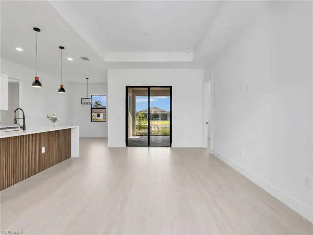 Open concept living space featuring light wood-finish flooring, a contemporary kitchen island with ribbed wood paneling, and modern pendant lighting
